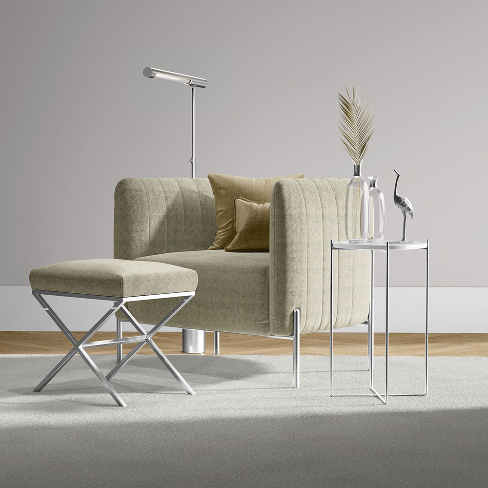 Beige tufted armchair with matching ottoman, chrome X-frame stool, glass-topped chrome tables, minimalist floor lamp.
