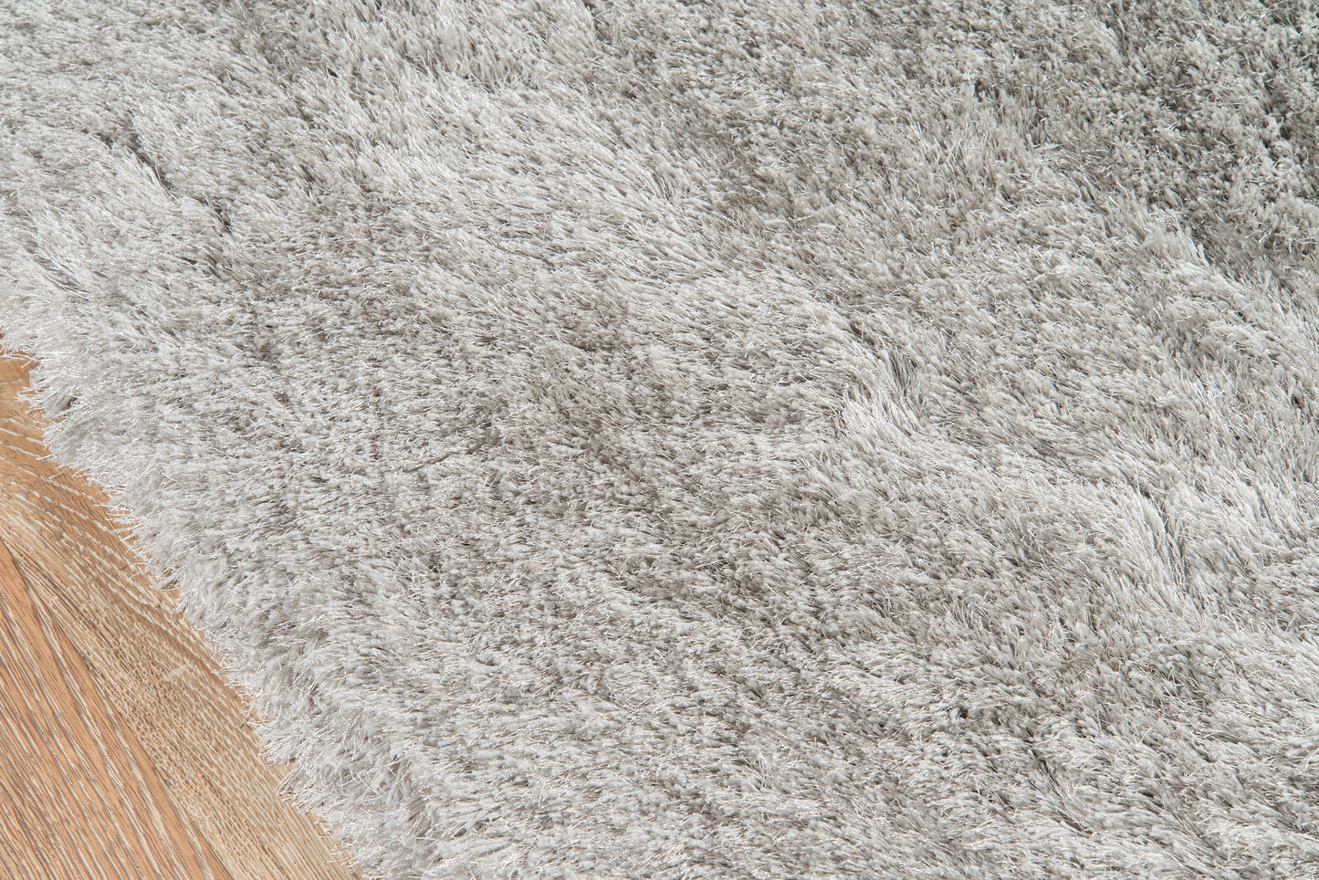 Light gray shag rug texture with brown wooden floor edge, cozy modern home decor.