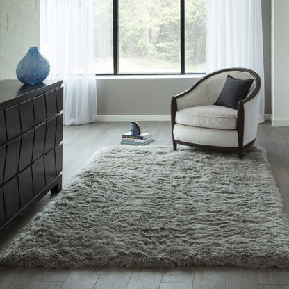 Light gray high-pile shag rug in a modern living room with a rounded beige armchair, dark wood dresser, blue vase.