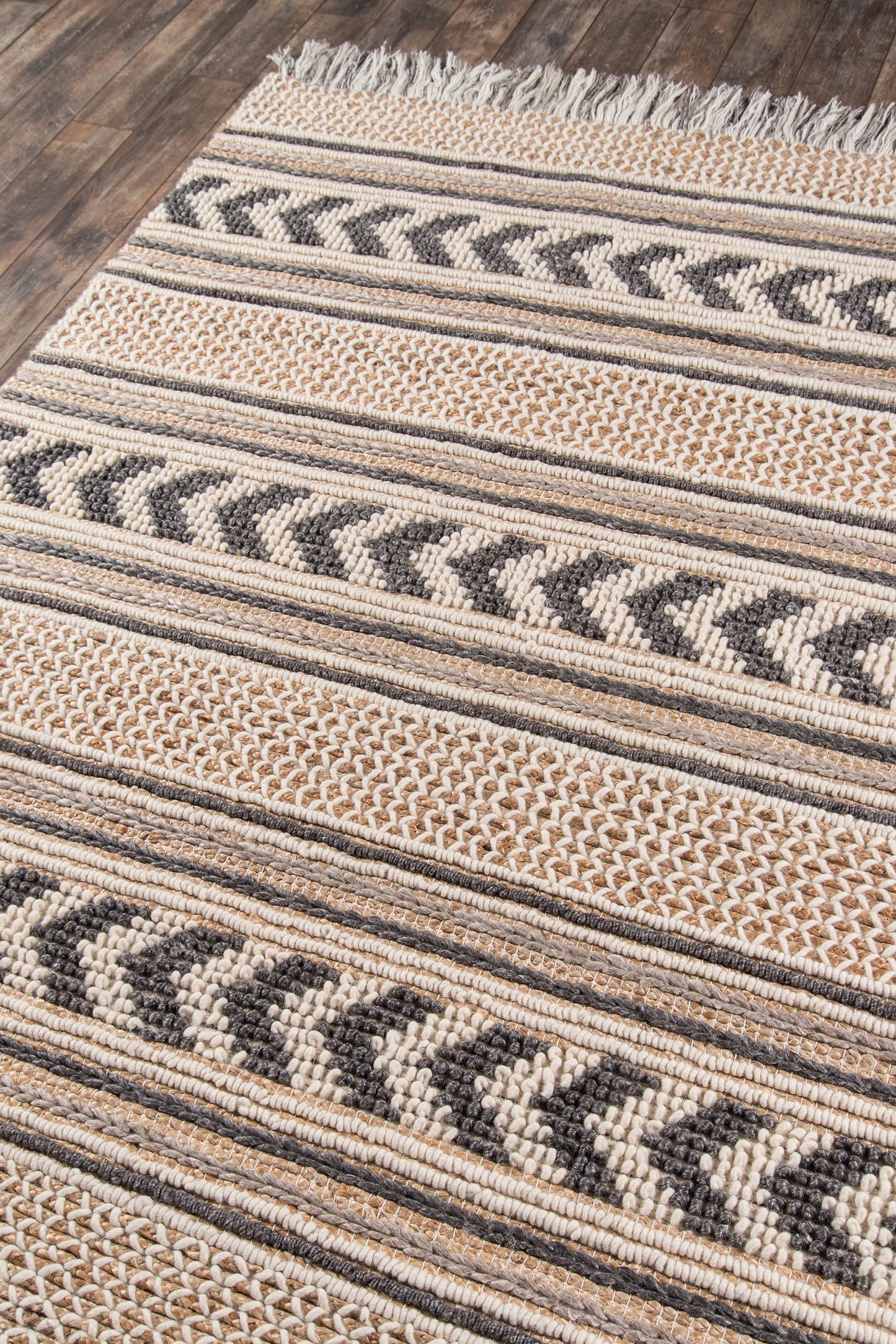 Beige and black striped woven rug with chevron motifs, fringe edge, on wood floor; rustic boho style.