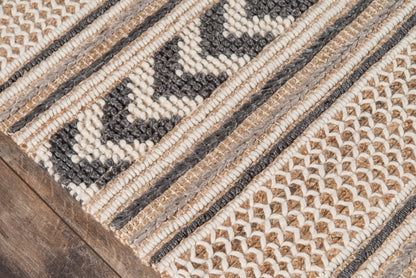 Beige, ivory and charcoal braided woven rug with chevron and geometric stripes on wood floor.