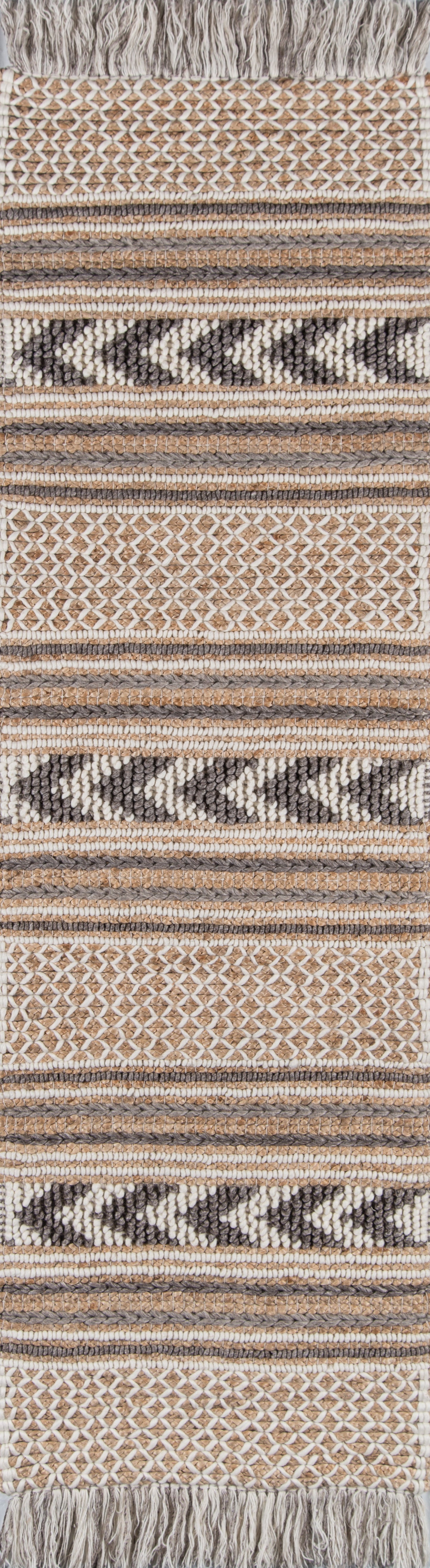 Woven rug featuring beige, cream, taupe and black geometric stripes, chevron and honeycomb motifs with a fringed top.