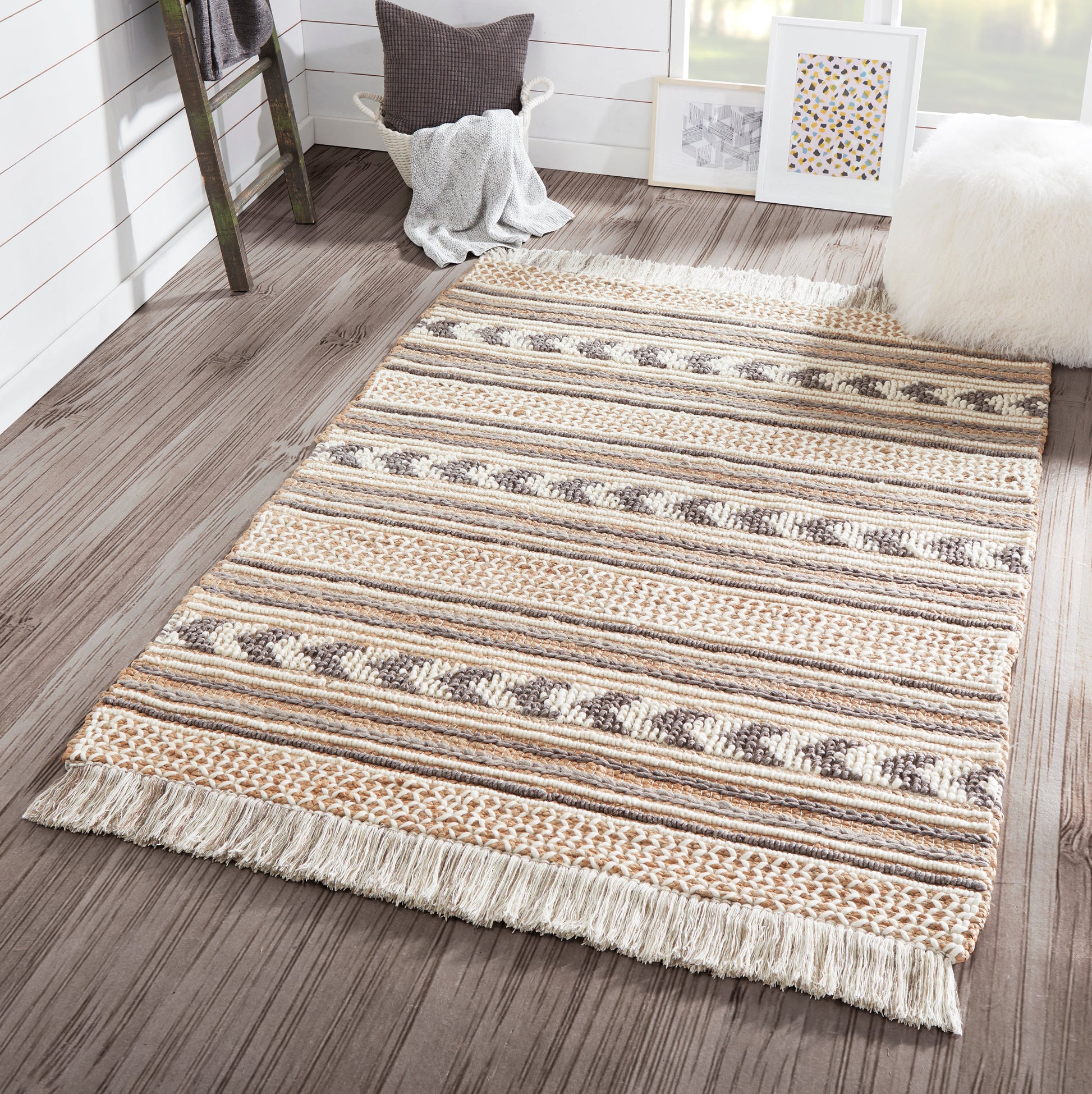 Rectangular woven rug with beige, tan and cream stripes, geometric motifs and fringed ends on a wood floor.