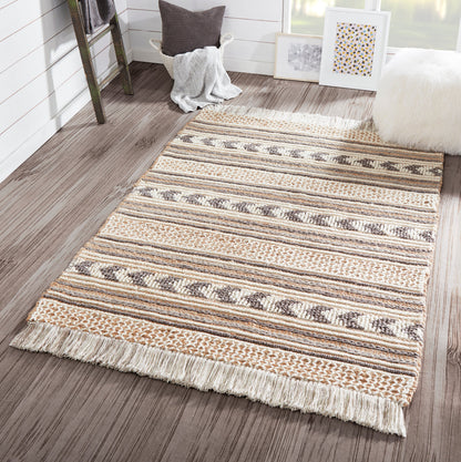 Woven striped area rug in cream, beige and brown tones with fringe ends, laid on dark wood floor in a cozy, modern room.
