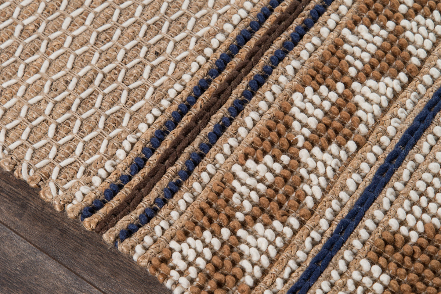 Close-up of a textured woven rug with beige, ivory and brown geometric pattern, navy borders and braided loops.