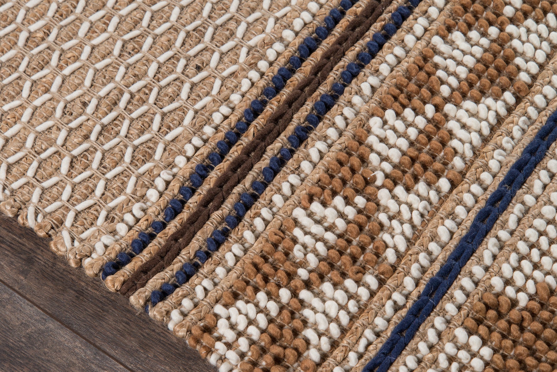Woven rug with beige base, brown and white geometric patterns, and navy border on a wooden floor.