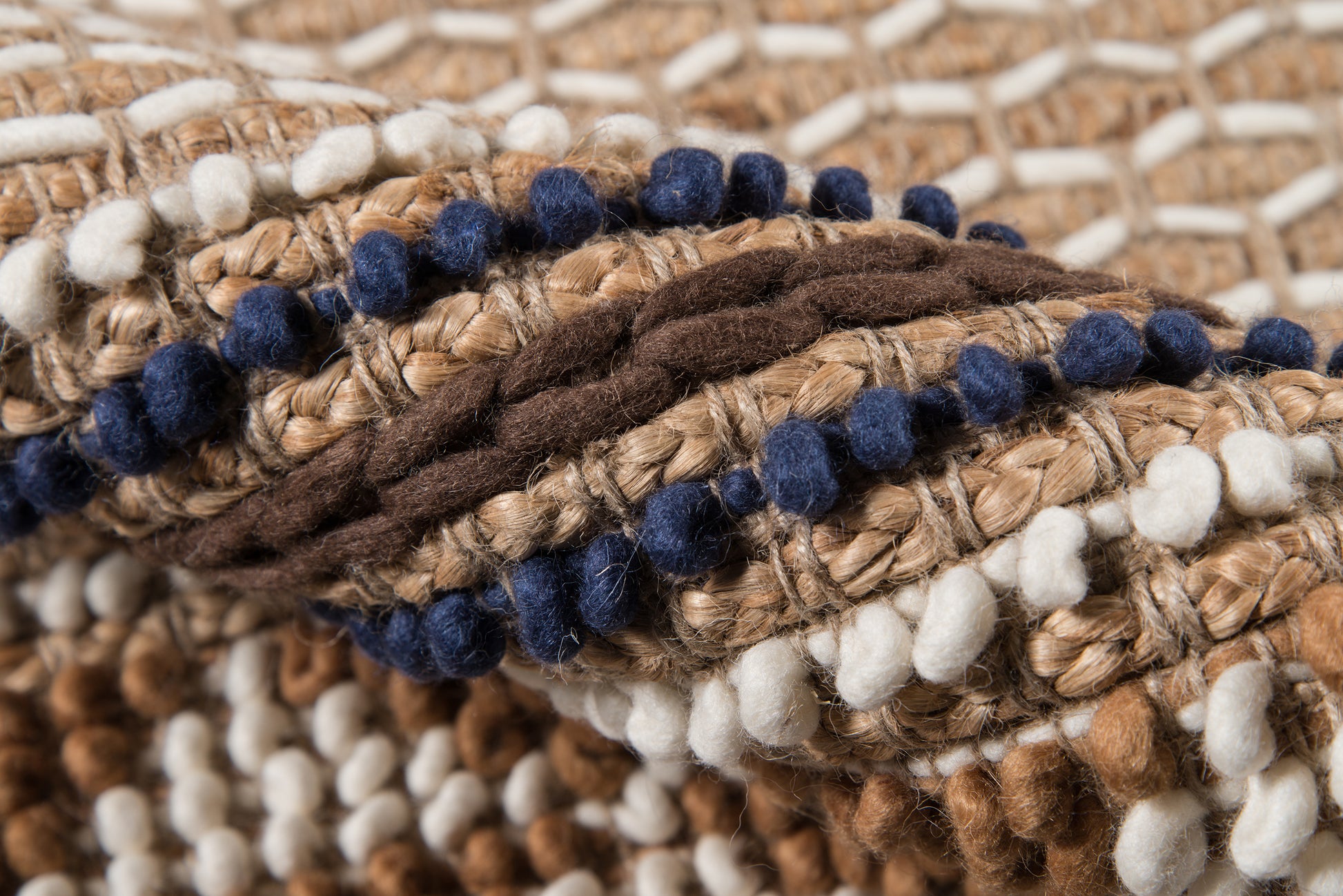 Close-up of chunky woven rug in beige, brown and white with navy blue pom-pom trim.