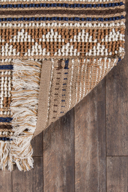 Beige-brown woven rug with white geometric diamonds, navy blue stripes, and fringed tassels on a dark wooden floor.