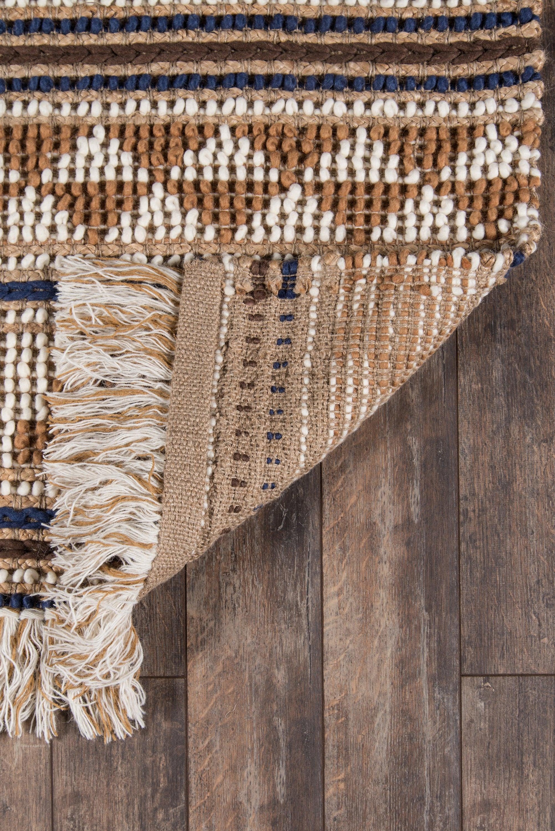 Handwoven rug in brown and ivory with white diamond motif, navy stripes, jute/cotton blend, fringe edge on wooden floor.