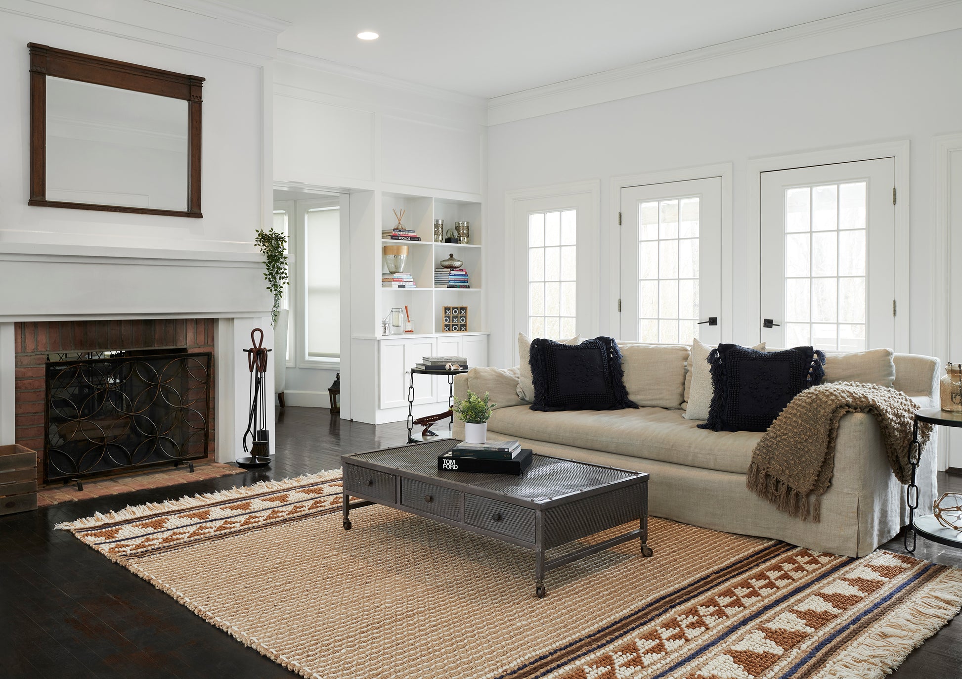 Bright white living room with beige sectional, navy pillows, taupe throw, dark metal coffee table, fireplace & shelves.