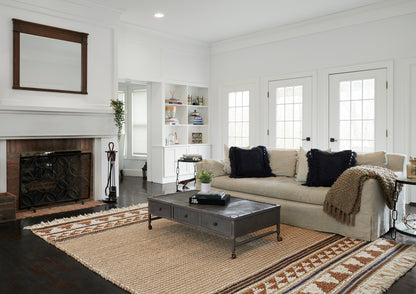 Bright modern living room with ivory sectional, navy pillows, dark wood coffee table, patterned runner rug, fireplace.