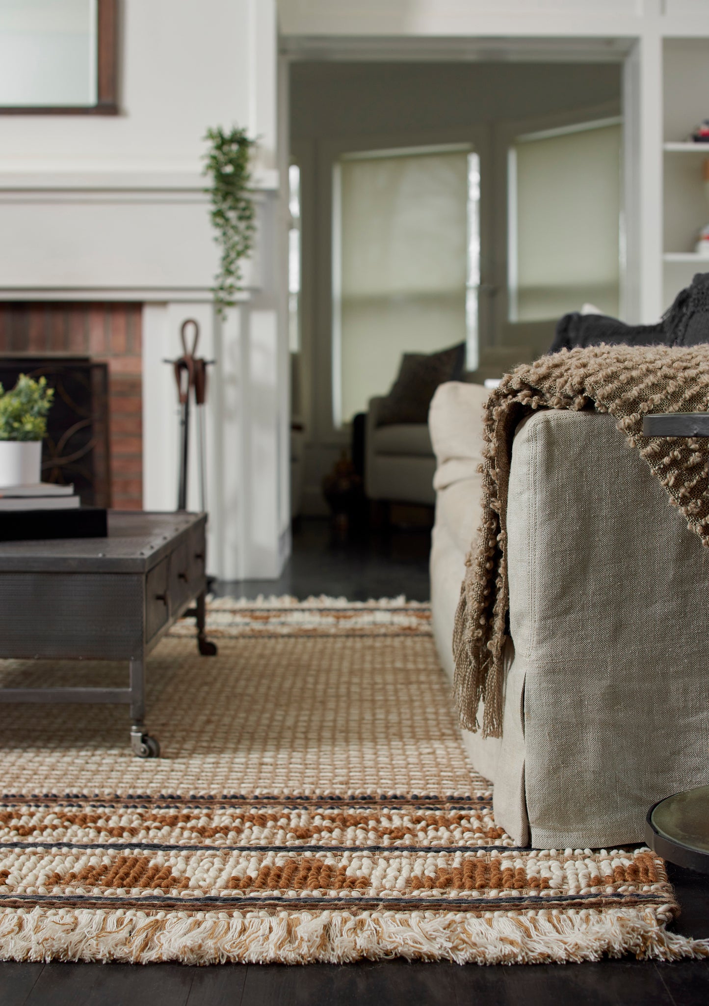 Cozy living room scene: beige sofa with chunky brown knitted throw, dark wood coffee table, and striped beige rug.