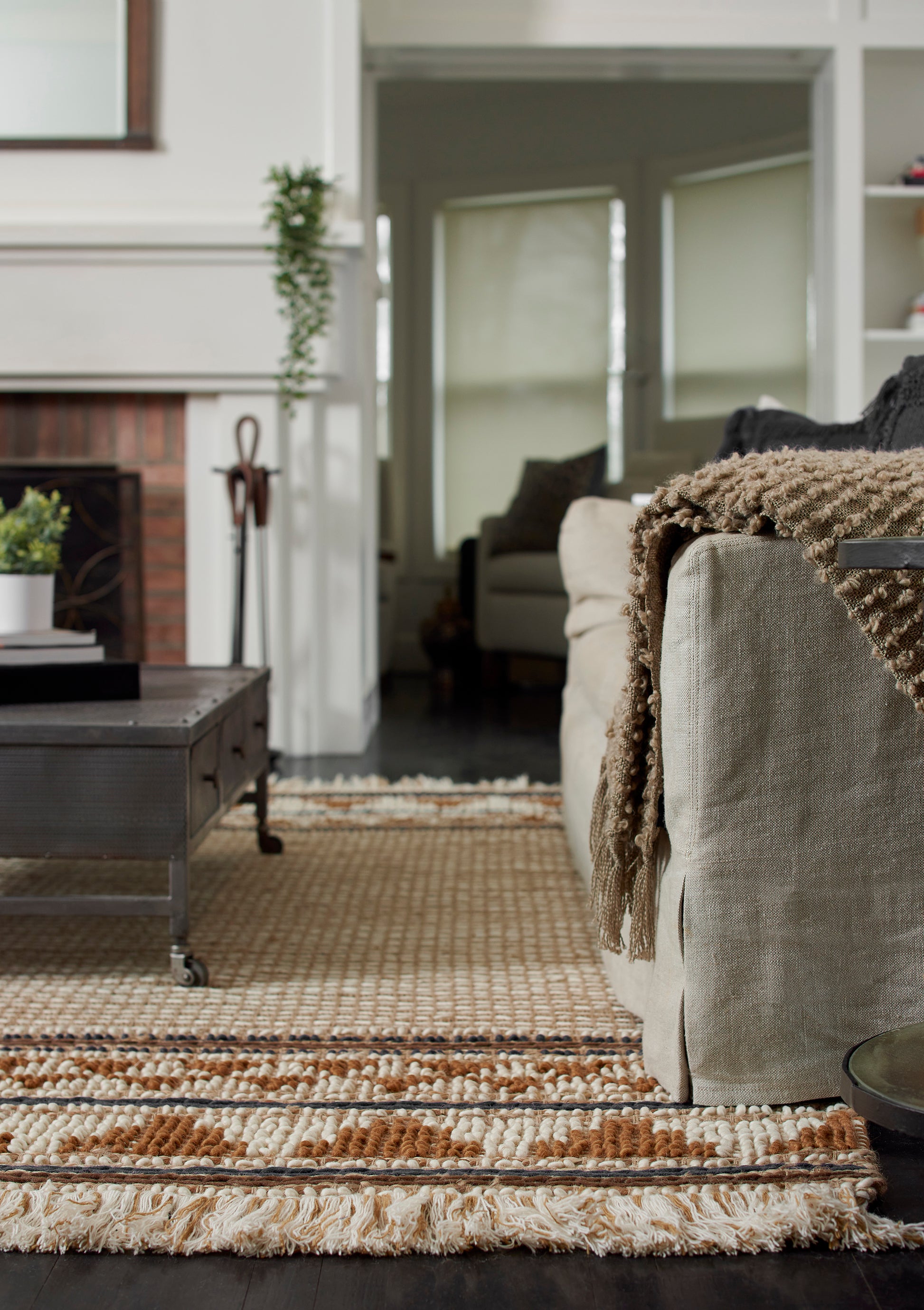 Cozy living room with beige sofa, chunky brown knit throw, woven striped rug, dark wood coffee table.
