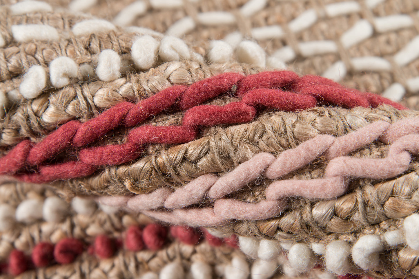 Close-up of a chunky braided yarn weave on a rug runner in beige, tan, pink and red tones.