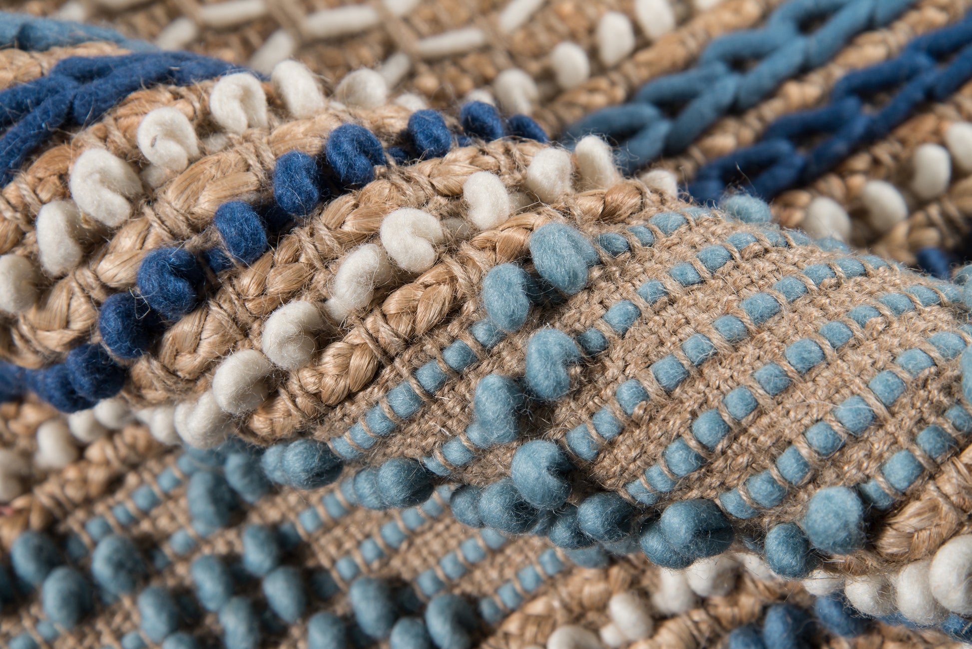 Close-up of a chunky woven textile in blues, beige and cream with pom-pom bobbles and textured stitches.