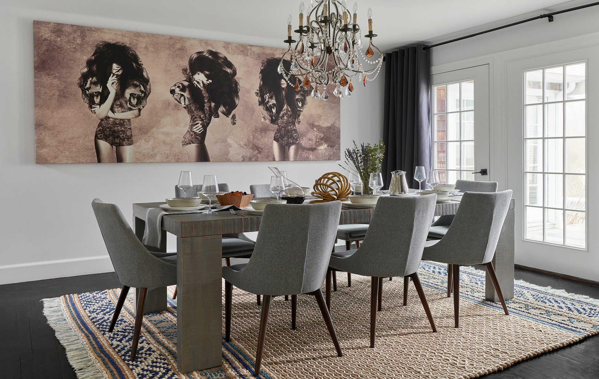 Rectangular dining room with grey upholstered chairs around a wooden table, chandelier, beige jute rug, and elephant artwork.