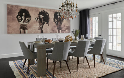 Gray upholstered dining chairs around a rustic wood table under a crystal chandelier on a blue-beige woven rug.