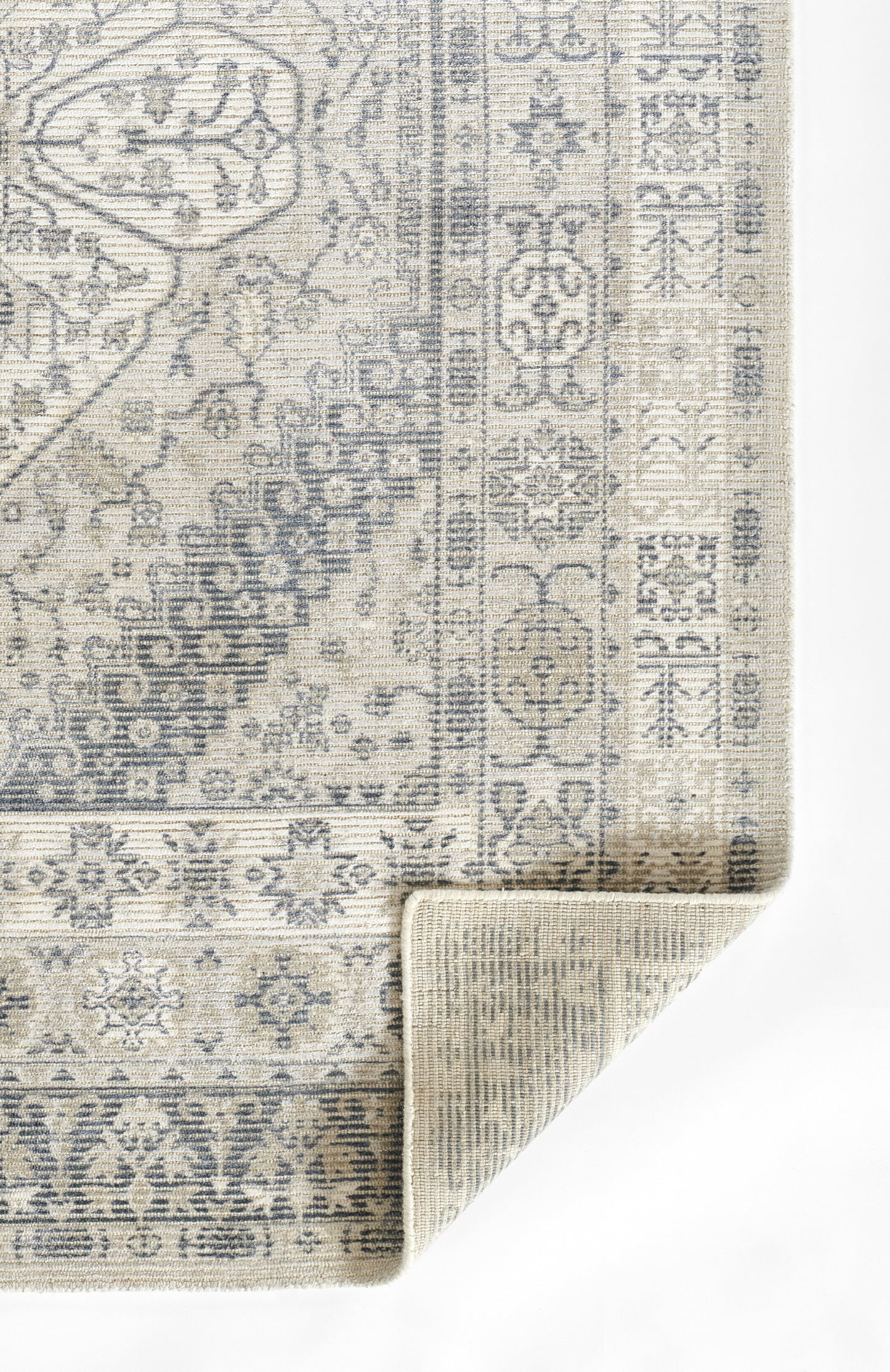 Grey distressed oriental-style area rug with intricate floral border and rolled corner.