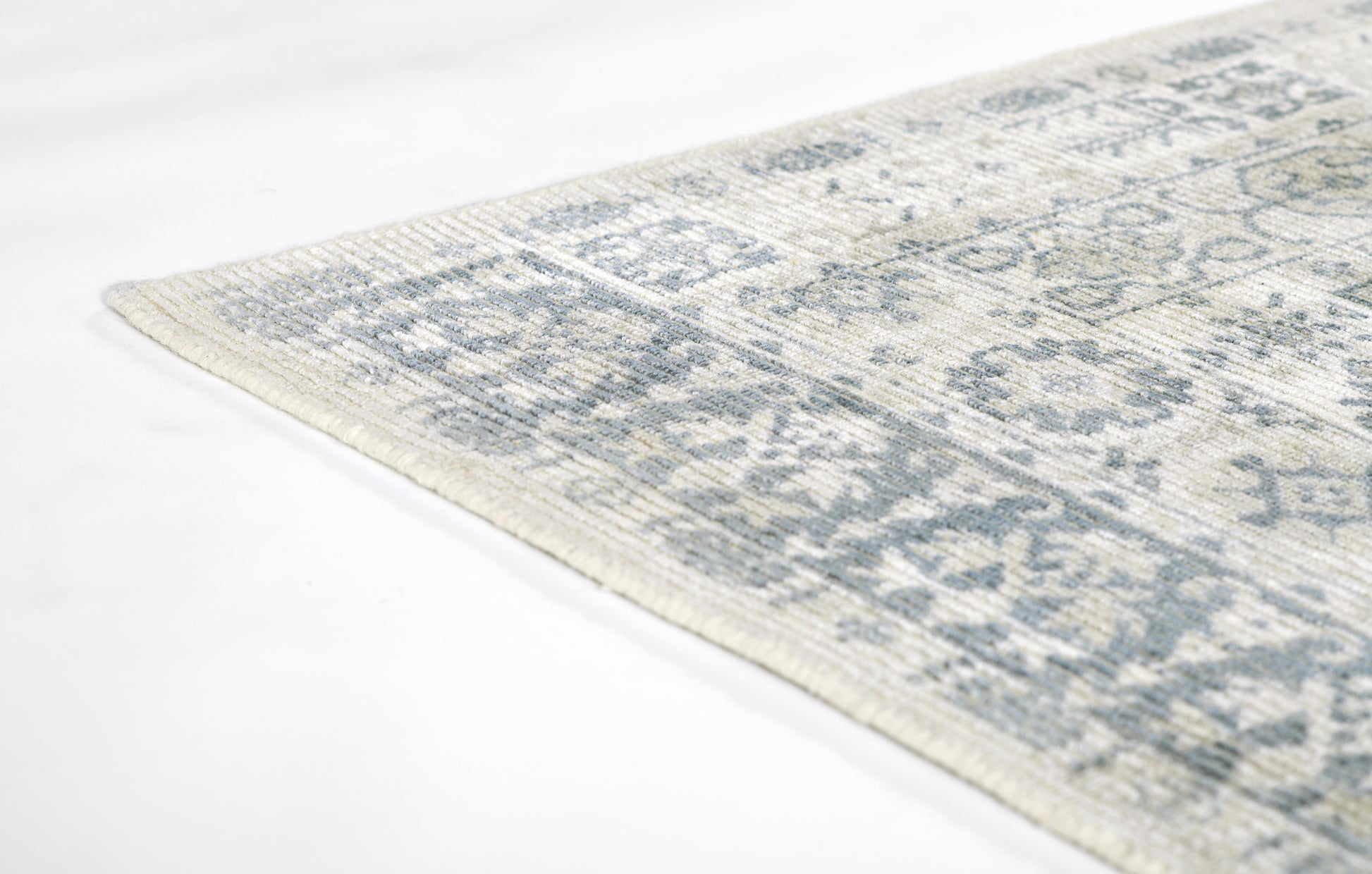 Light ivory and gray oriental rug with distressed blue-gray floral motifs; corner view.