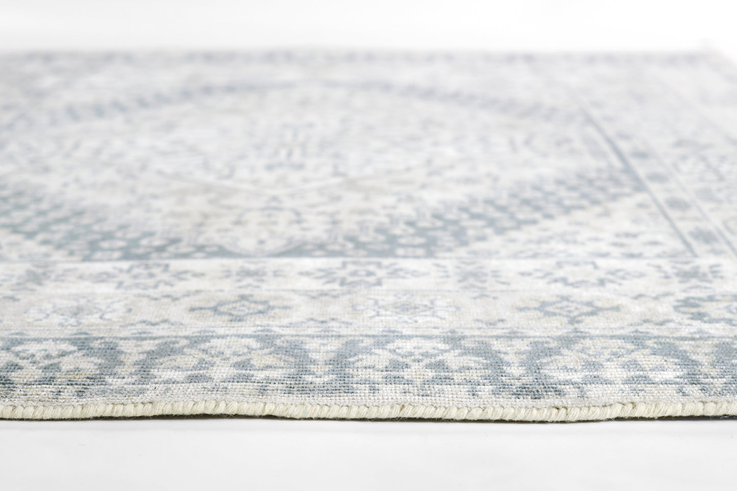 Light gray-blue patterned area rug with a faded central medallion and fringed edge.