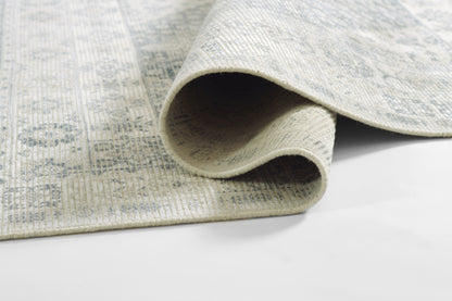 Light gray woven rug with a subtle blue pattern, rolled edge, and a soft texture for contemporary living spaces.