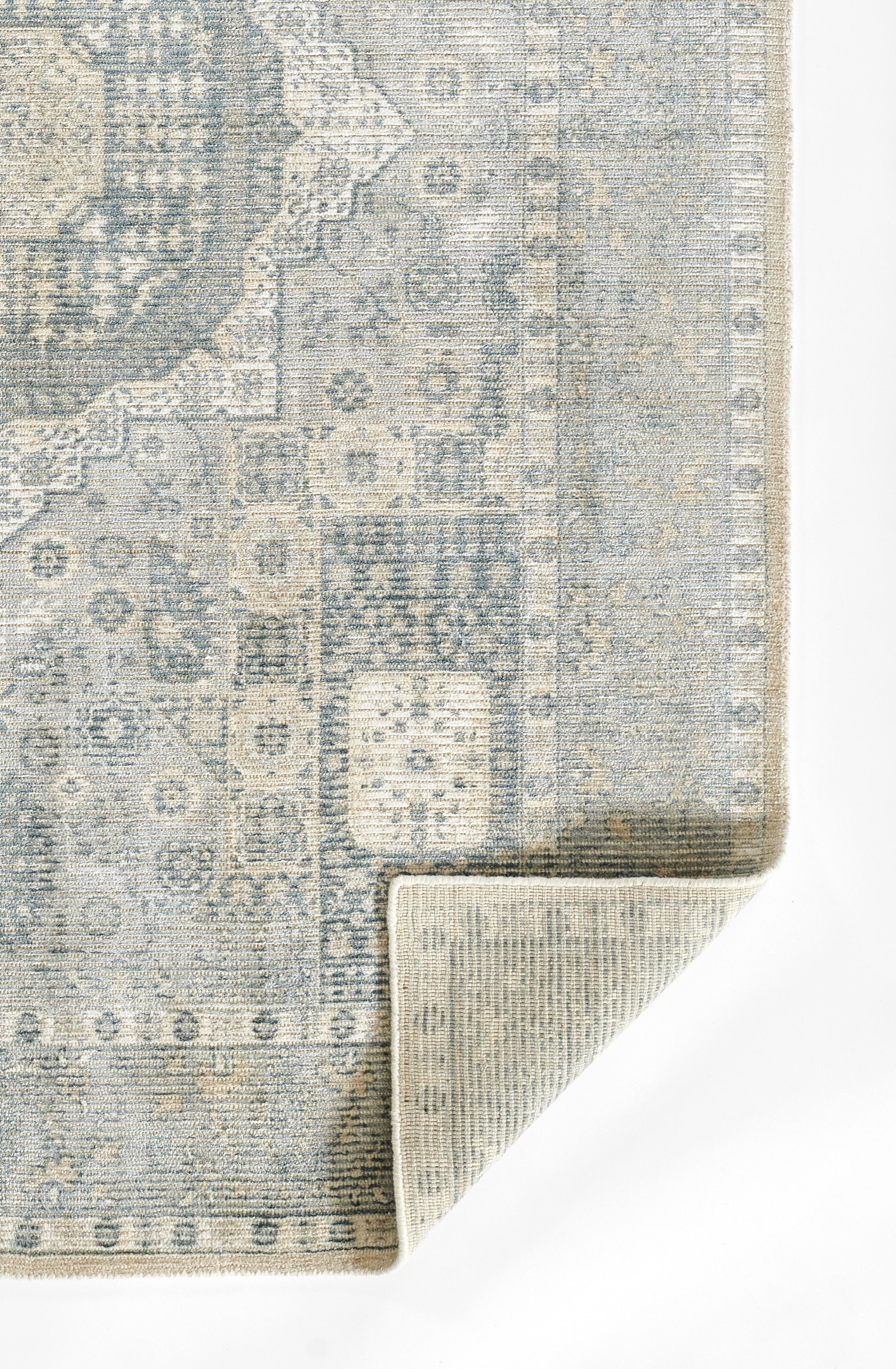 Blue-grey distressed oriental rug with intricate geometric floral pattern; folded corner reveals beige underside.