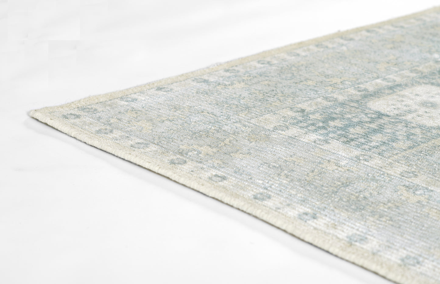 Light blue-gray distressed area rug with soft vintage pattern, low-pile, corner view.