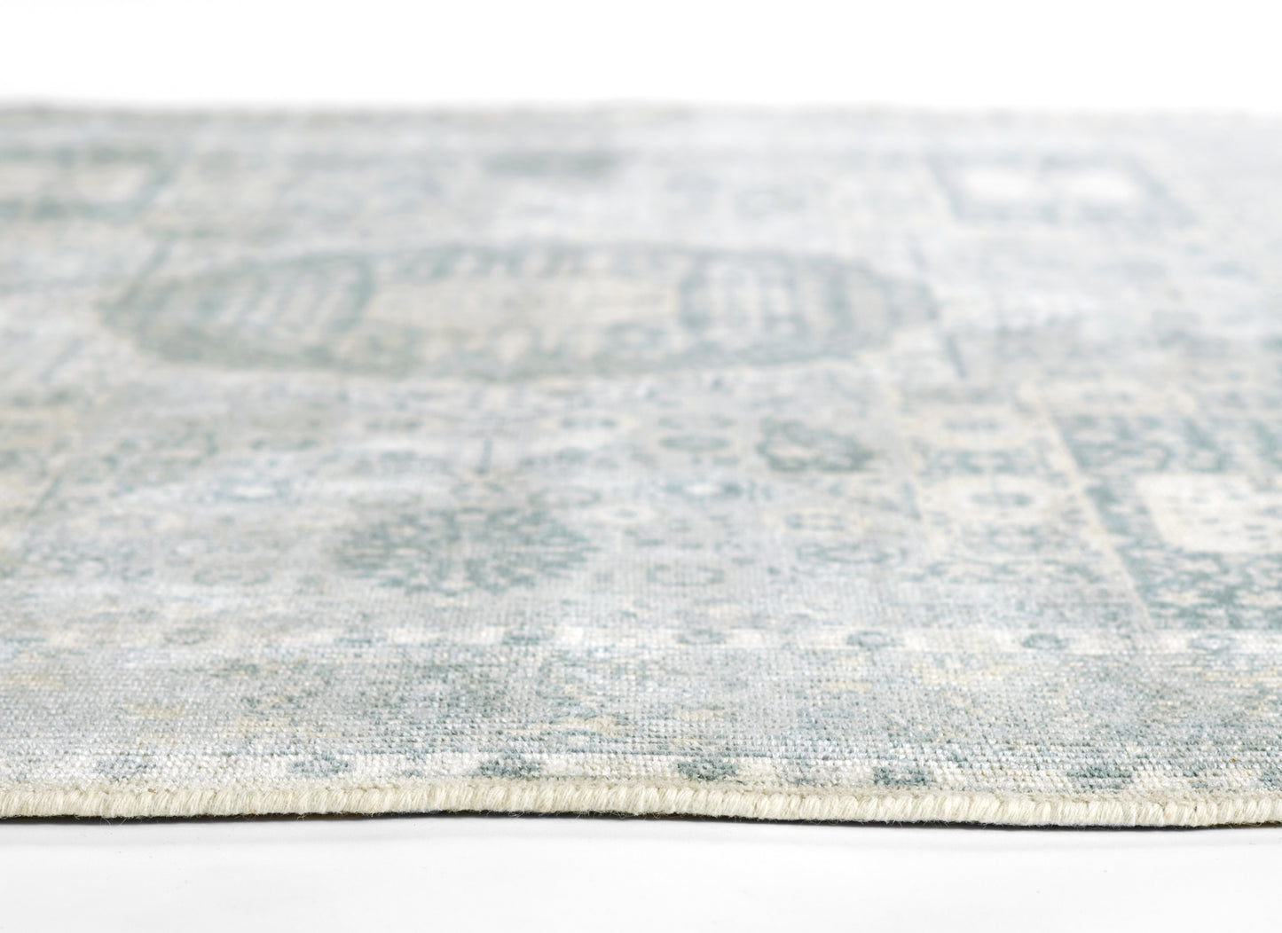 Blue-gray rug with faded geometric motifs, soft flatwoven texture, light fringe along the edge.