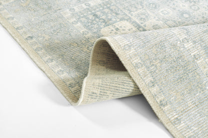 Blue-gray patterned rug with woven texture and a rolled edge revealing its beige underside.