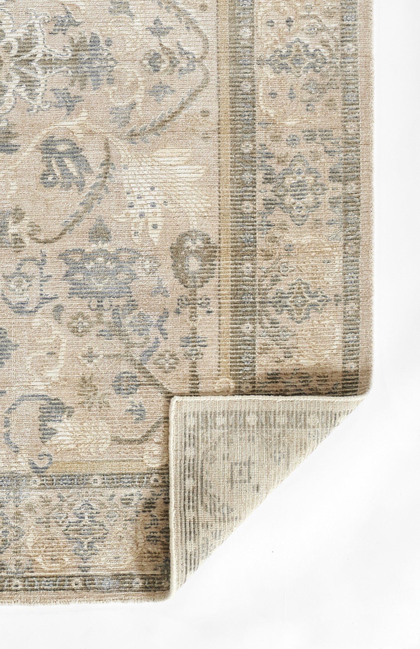 Beige & light-blue traditional area rug with floral motifs & ornate border; corner folded to show backing.