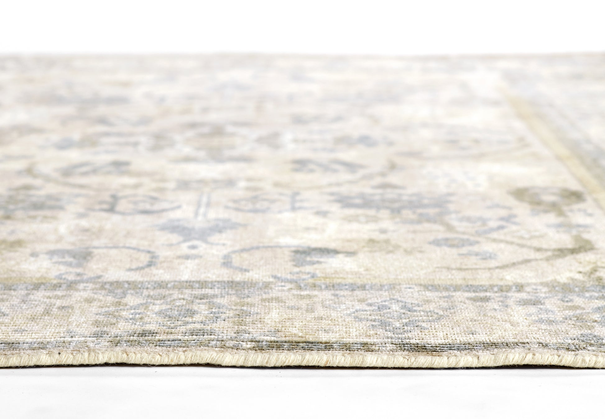 Beige vintage-style oriental rug with faded blue-gray floral medallion pattern and low pile, edge view.
