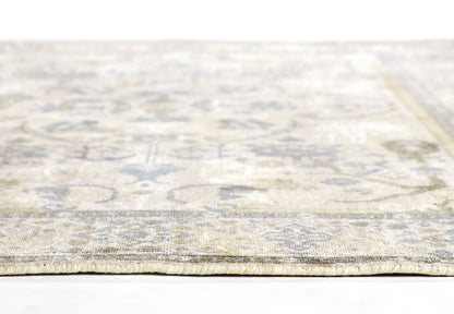 Beige vintage-style oriental rug with faded blue-gray floral medallion pattern and low pile, edge view.