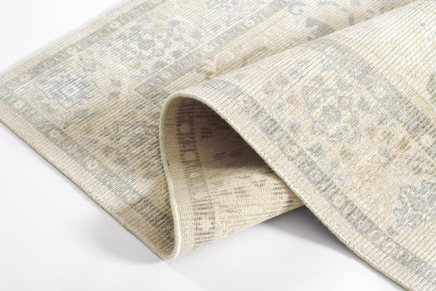 Beige distressed woven rug with faded blue-gray oriental motifs and a rolled edge.