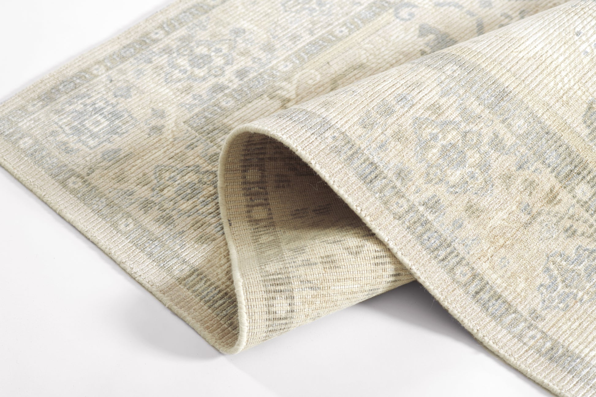 Beige distressed woven rug with faded blue-gray oriental motifs and a rolled edge.