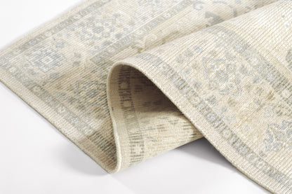 Beige distressed woven rug with faded blue-gray oriental motifs and a rolled edge.