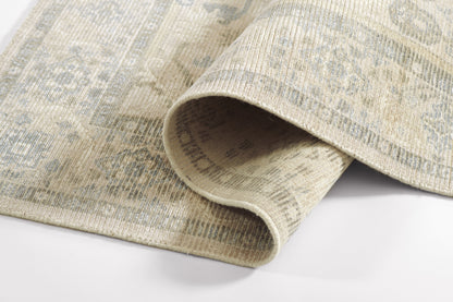 Beige distressed area rug with blue-gray motifs; rolled edge reveals soft woven pile.