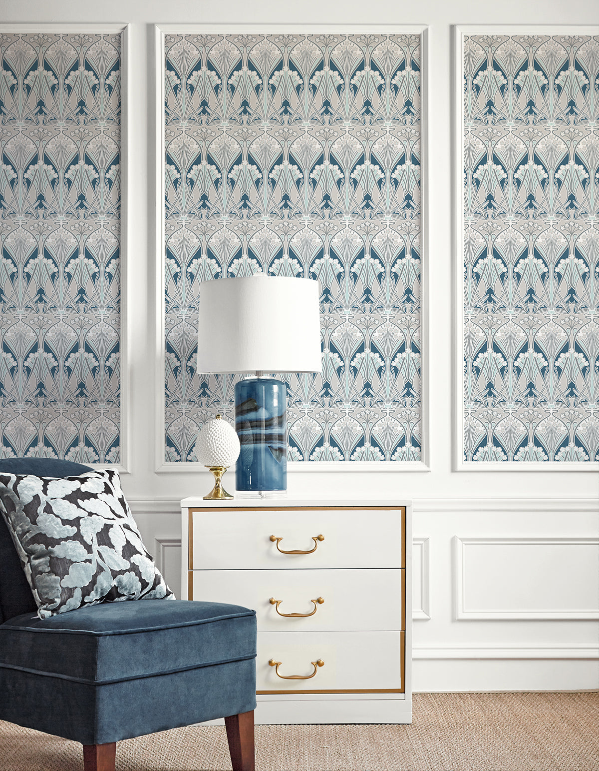 Blue damask wallpaper triptych, white dresser with gold handles, blue glass lamp, decor orb, navy velvet chair