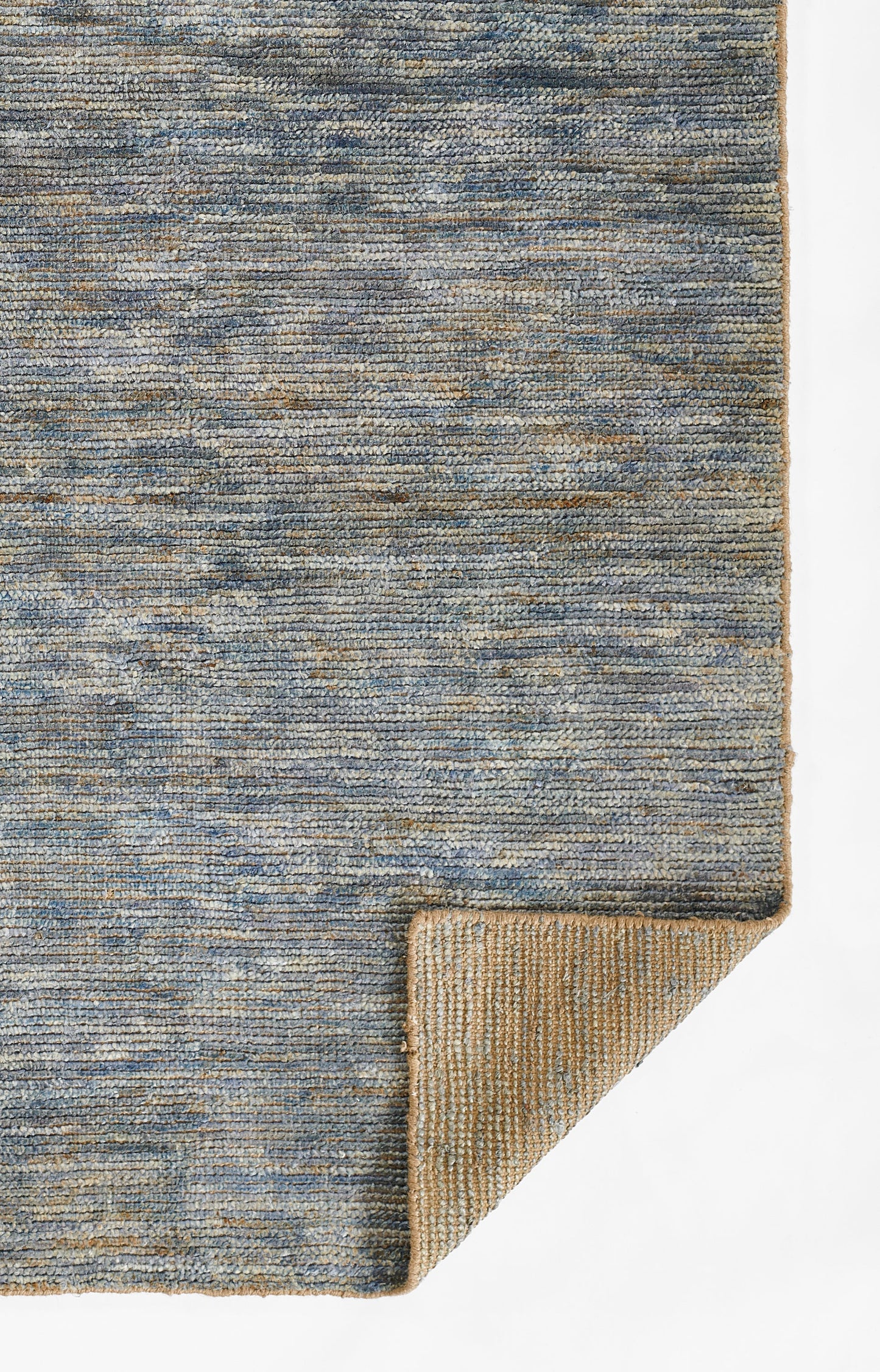 Blue-gray flat-weave rug with subtle texture; corner turned up to reveal tan underside.