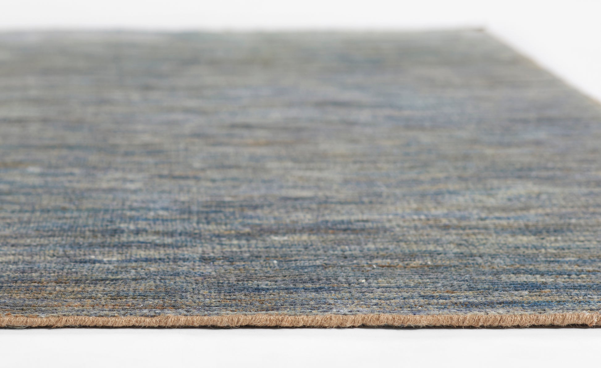 Blue-toned woven rug close-up with textured surface and tan binding edge.