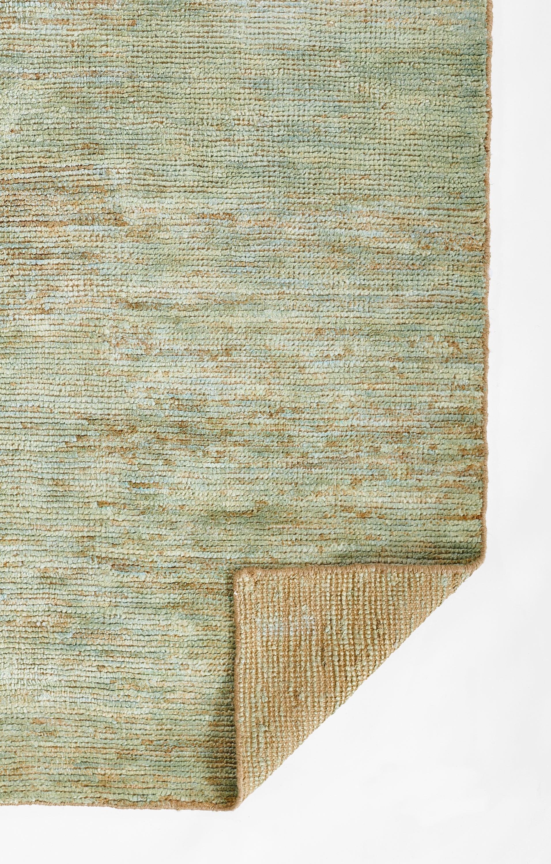 Green-teal textured rug with a subtle distressed pattern; folded corner reveals beige underside.