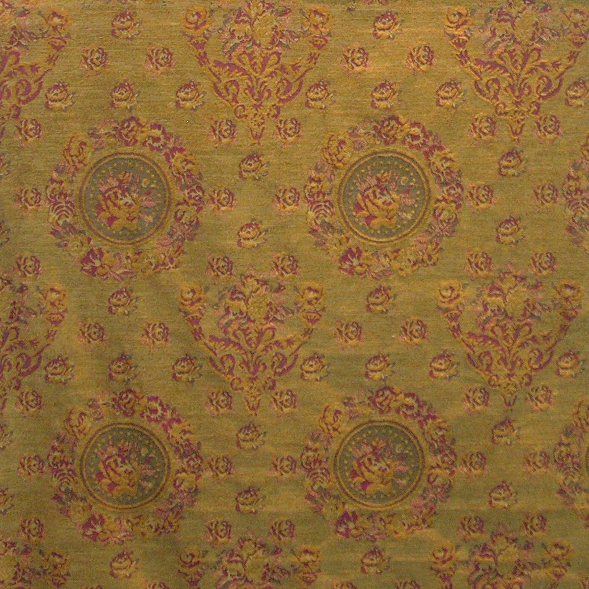 Dijon-colored fabric with pink and gold damask motifs and circular floral medallions, ornate upholstery texture.