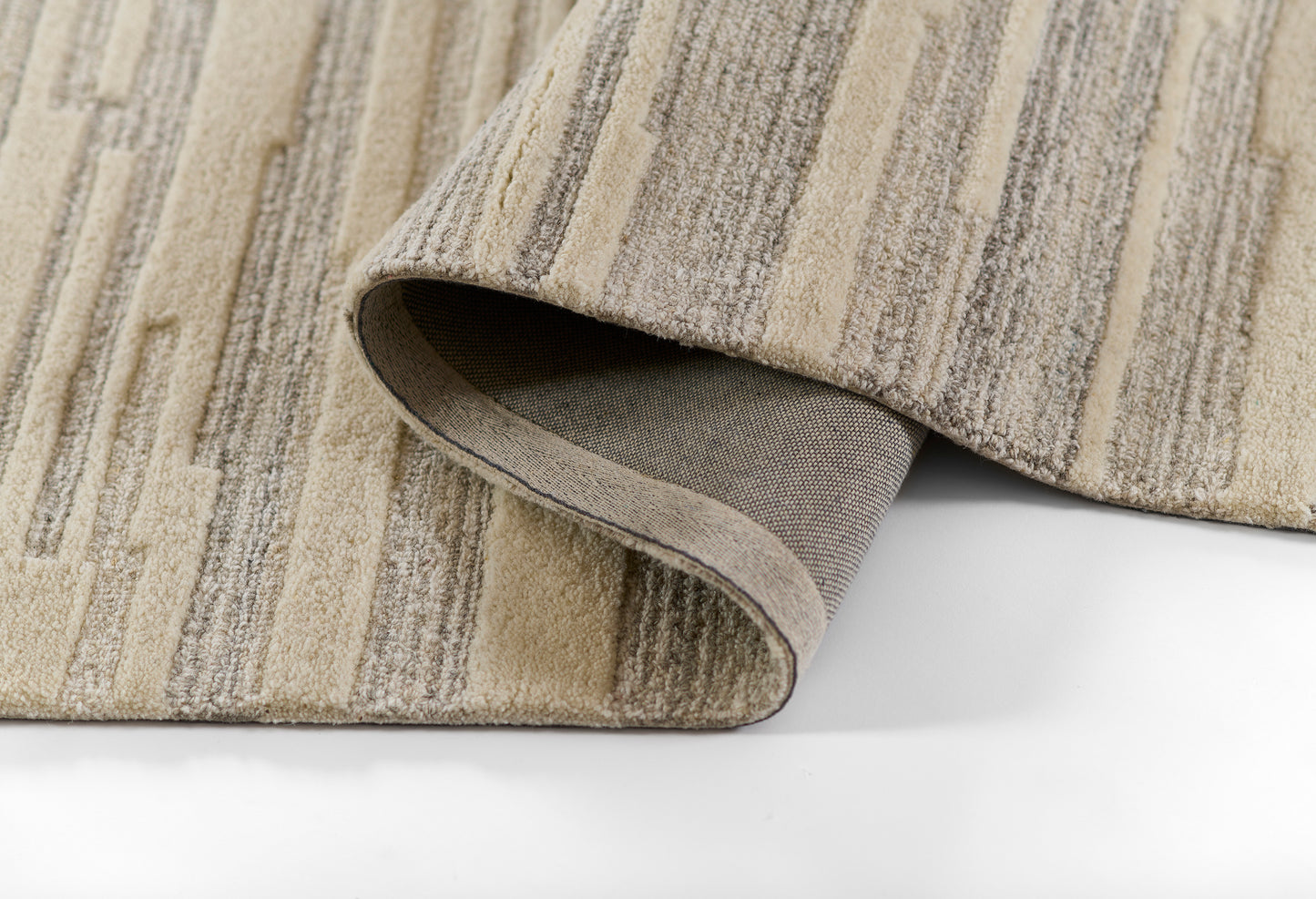 Gray-beige striped area rug, soft woven pile; folded corner reveals underside, modern home decor.