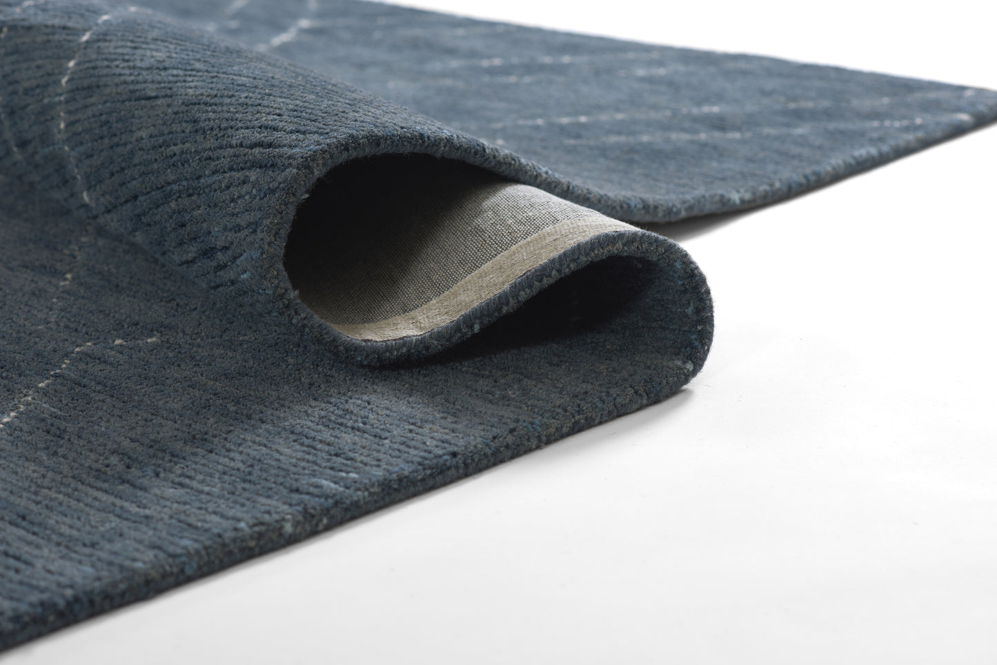 Dark blue textured rug with rolled edge, beige underside visible; denim-like weave.