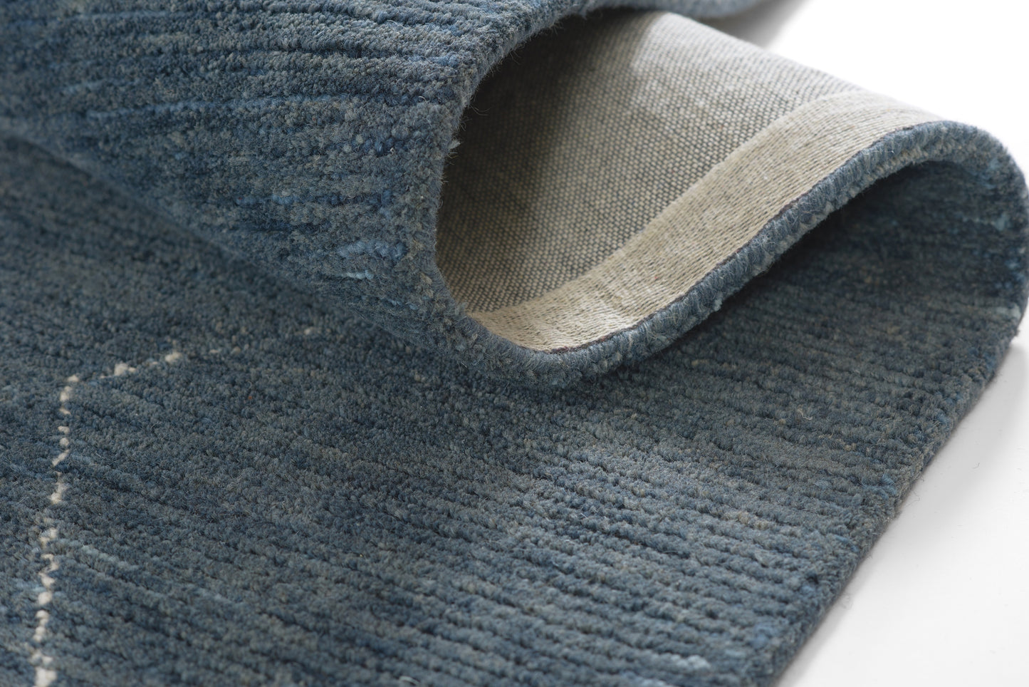 Blue textured rug with beige underside and rolled edge.