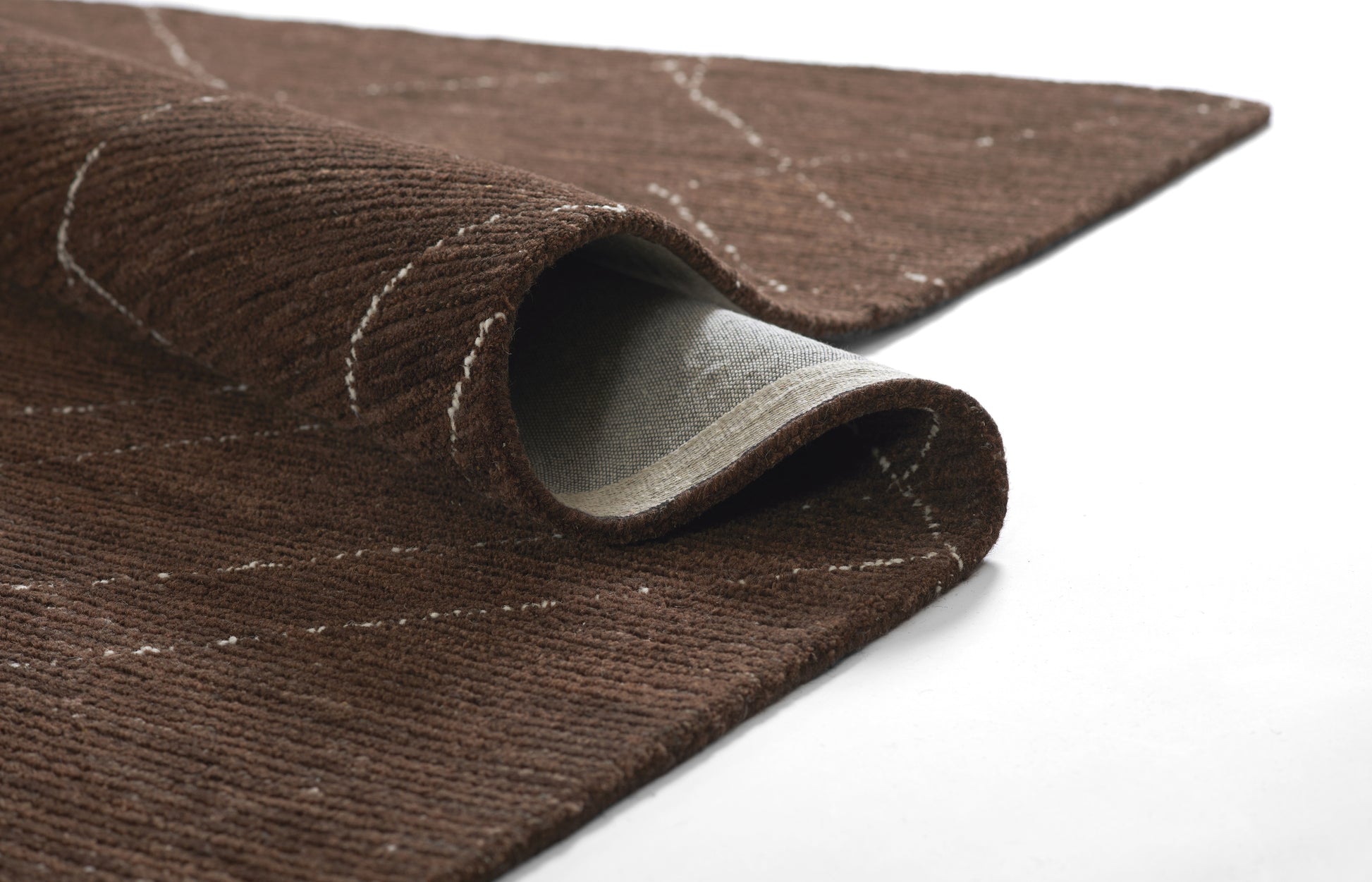 Brown textured rug with light cream dashed lines, folded corner shows gray backing; plush, modern living room decor.