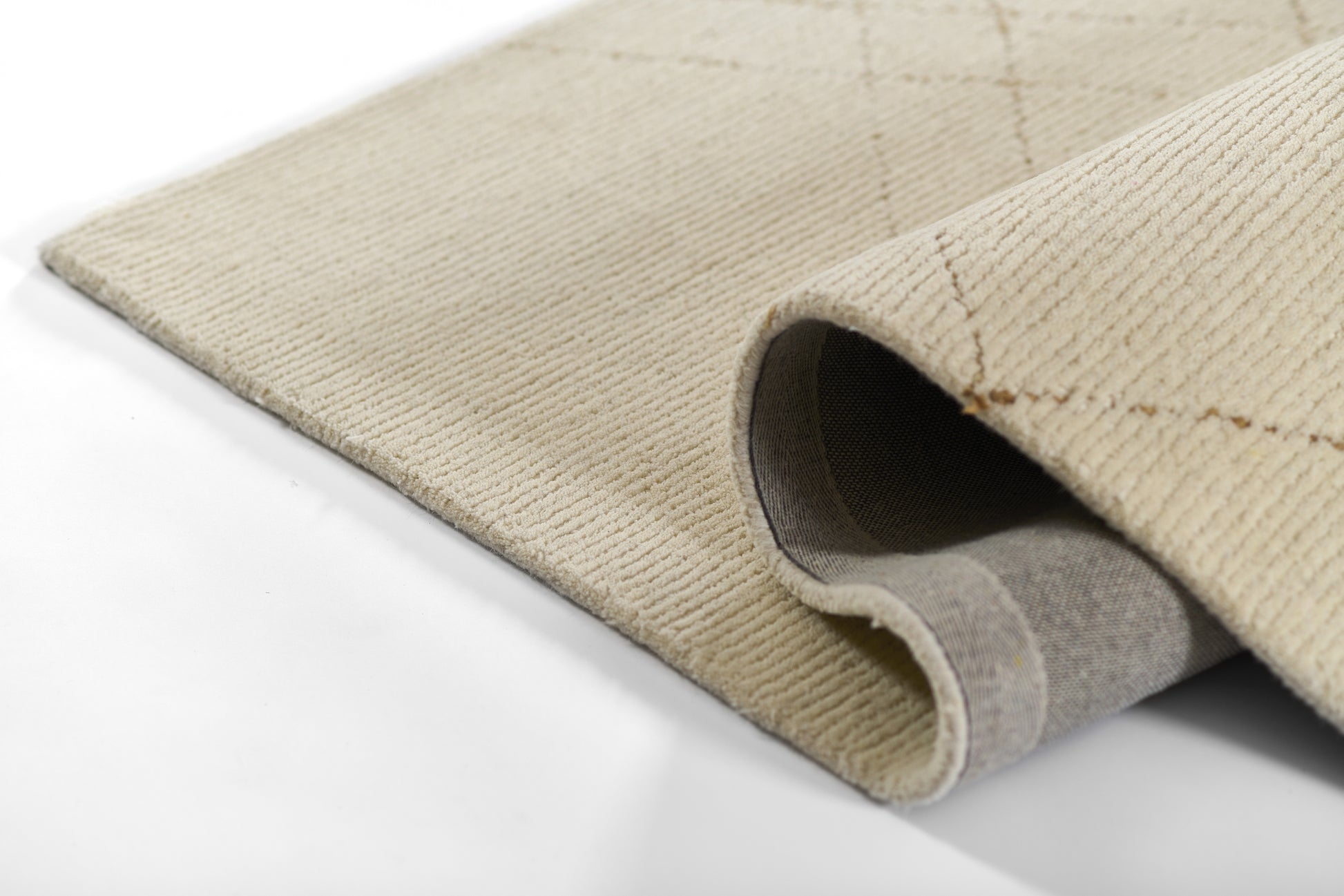 Beige woven rug with soft pile and gray backing, rolled edge showing texture.