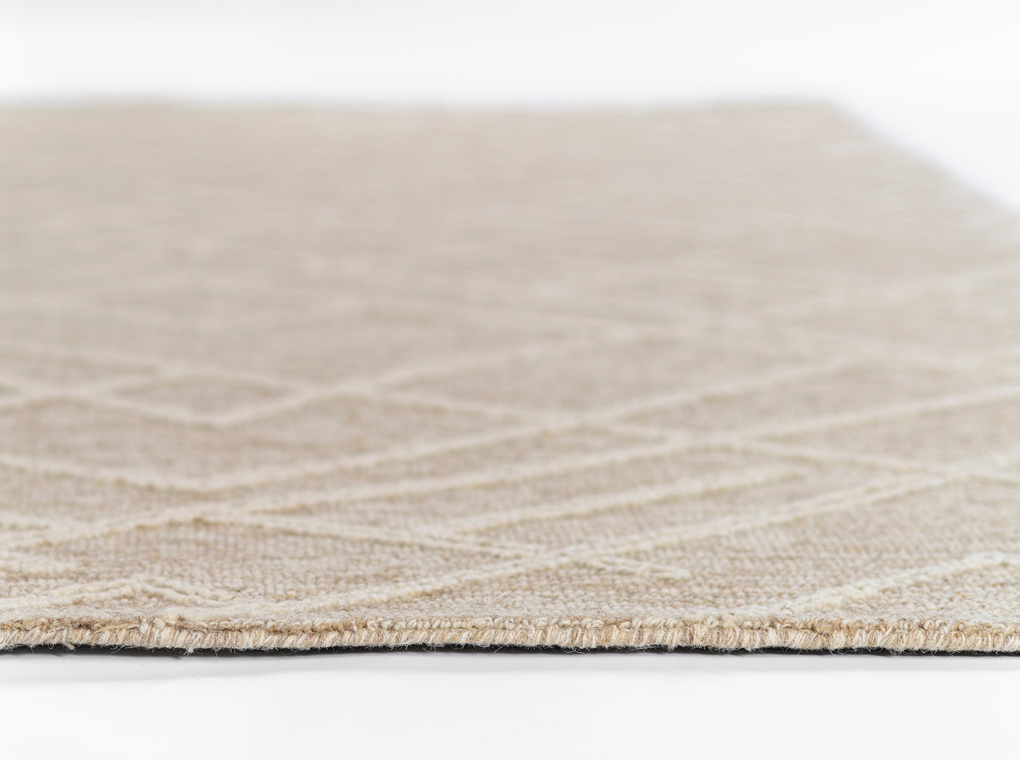 Natural beige woven rug, close-up edge view showing subtle geometric pattern and low pile.