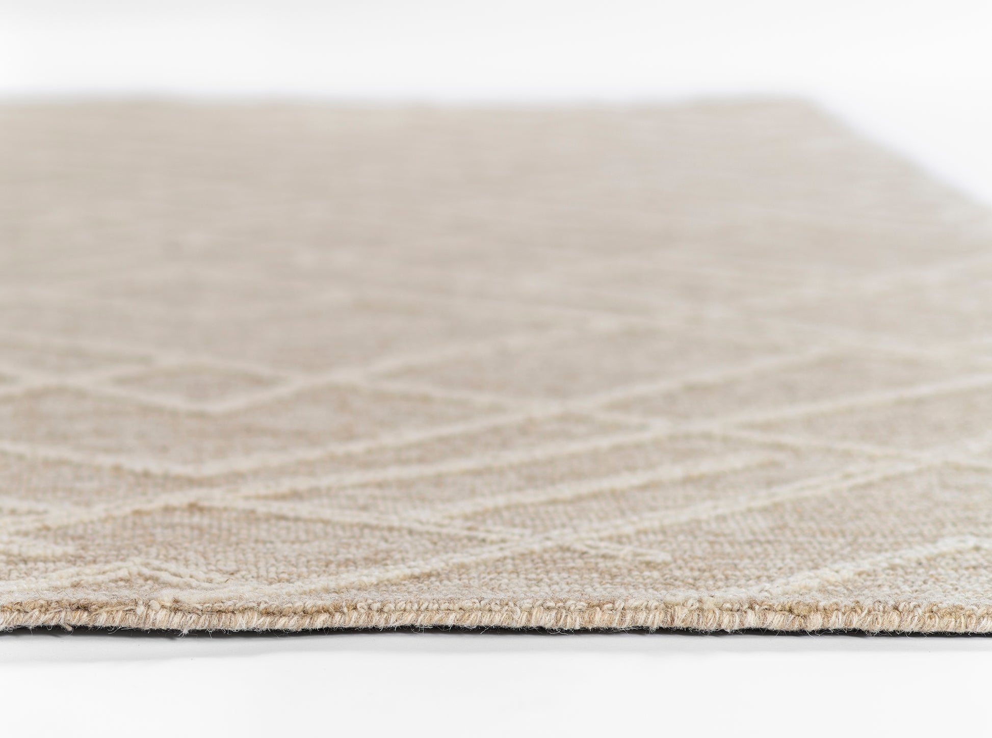 Natural beige woven rug, close-up edge view showing subtle geometric pattern and low pile.