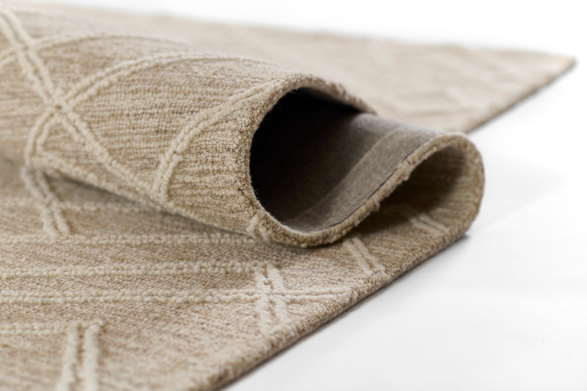 Beige woven area rug with geometric pattern, soft loop pile, rolled edge showing underside.