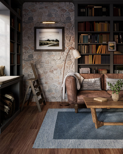 Cozy living room with stone wall, brown leather sofa, wooden coffee table, blue rug, floor lamp, & tall bookcase.